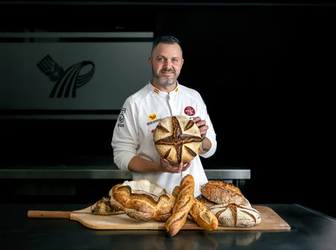 Yohan Ferrant holding a scored sourdough loaf above a board of baguettes and country breads
