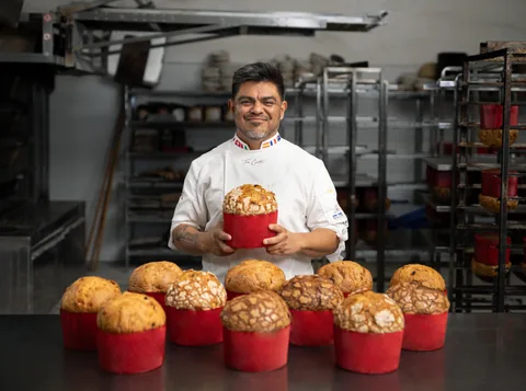 Ton Cortés holding a panettone above a table of freshly baked panettoni in red paper moulds