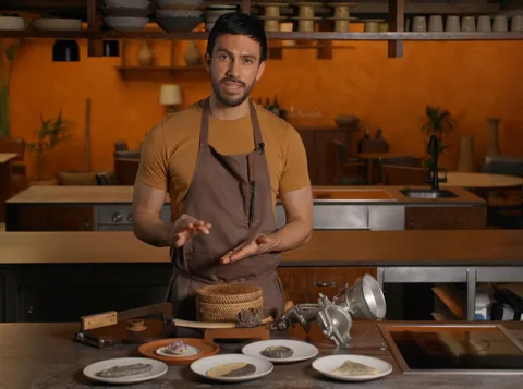 Santiago Lastra in a brown apron behind a board of masa preparations, a basket of tortillas and a hand grinder