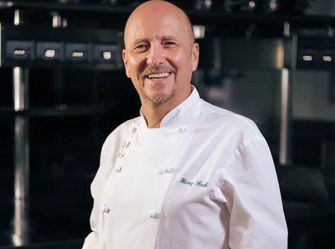Heinz Beck smiling in his chef whites in a professional kitchen